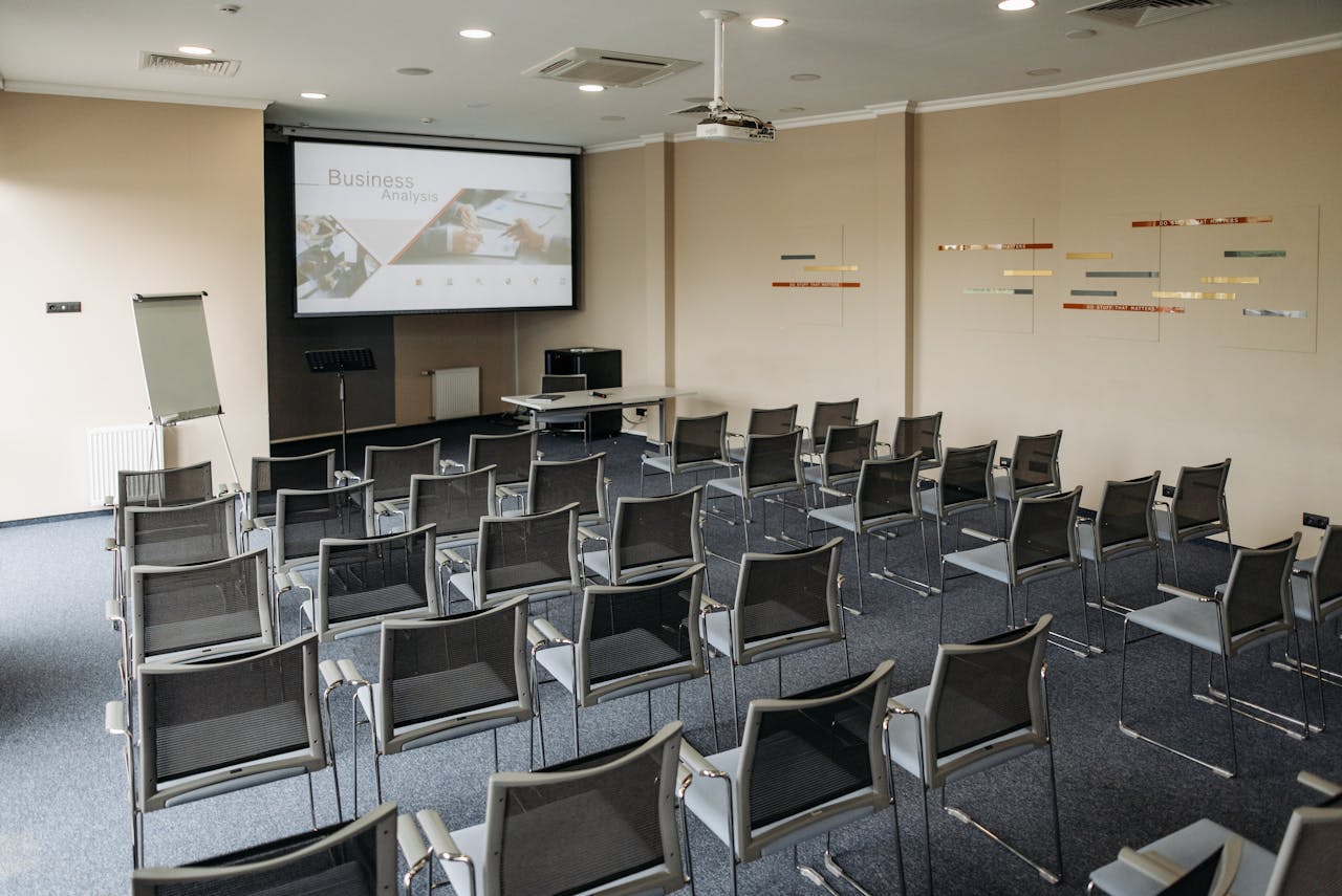Empty conference room featuring rows of chairs, screen, and whiteboard.