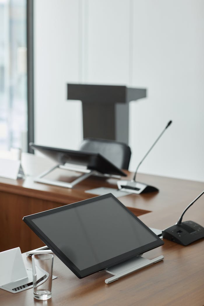 A contemporary conference room setup featuring digital tablets and microphones on a wooden table.